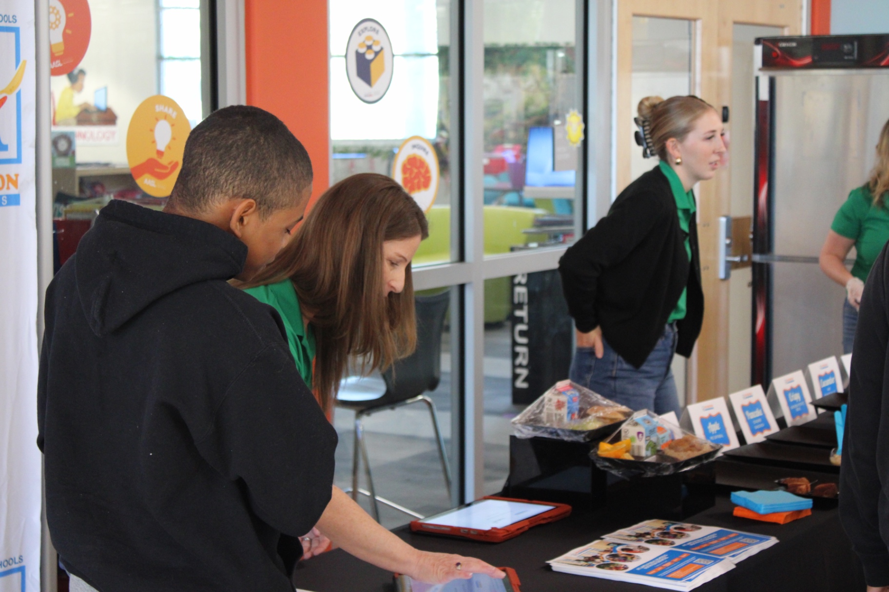 A student and APS staff member using a MealViewer tablet beside displayed menu samples