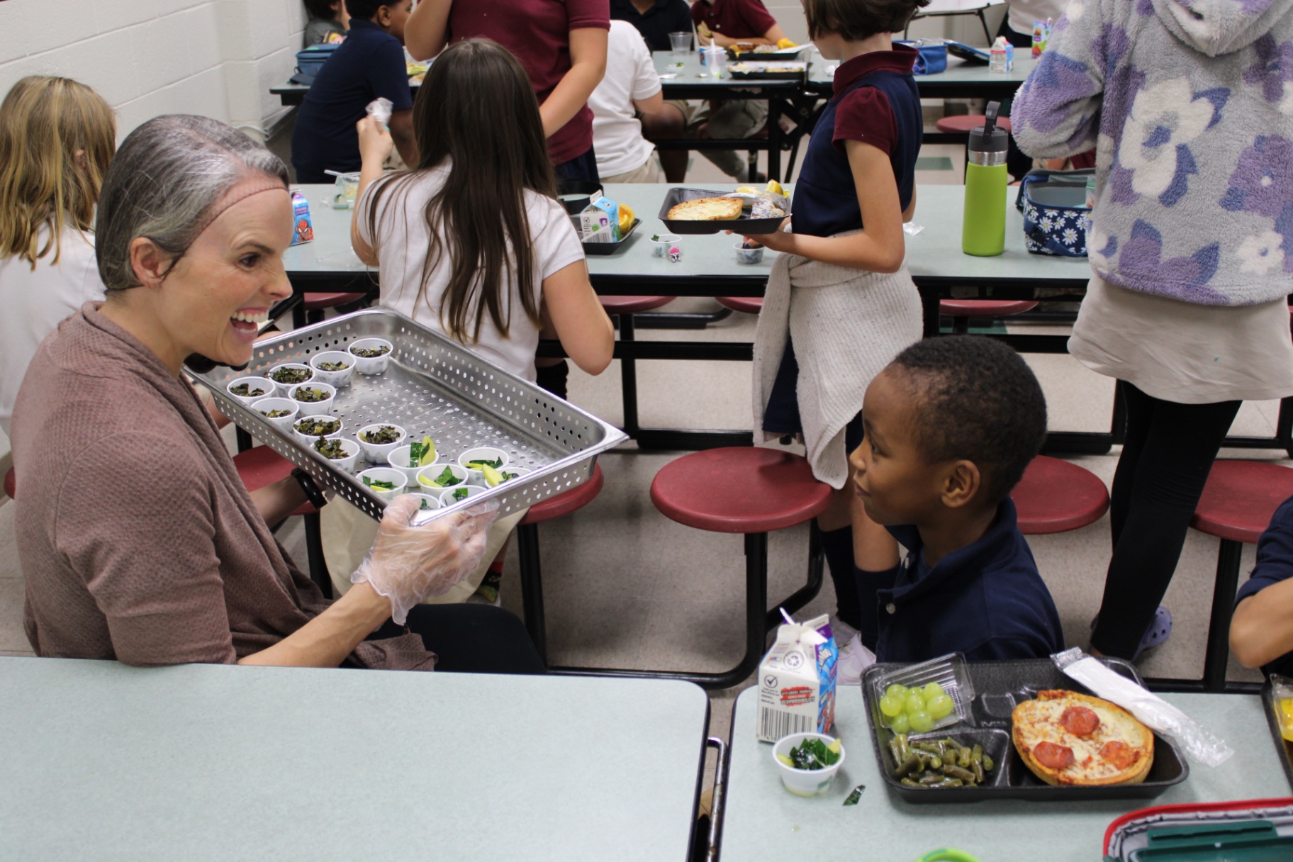 APS cafeteria team member offering a student samples of leafy greens during lunch